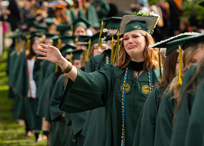 A tearful graduate waves while walking to her seat during the processional.