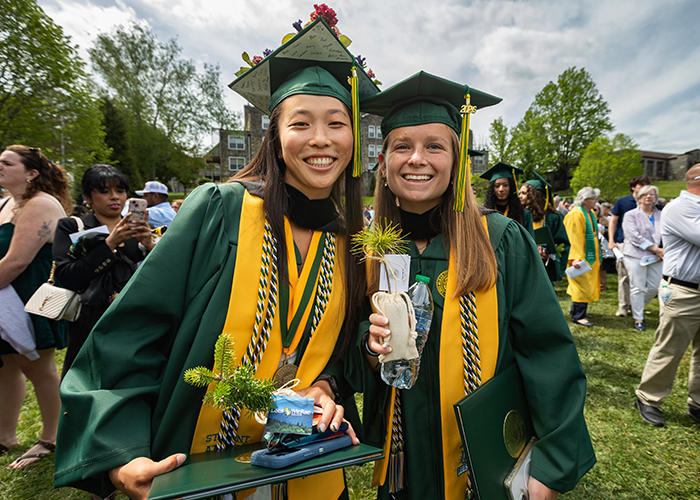 Two graduates pose together and smile while holding saplings.