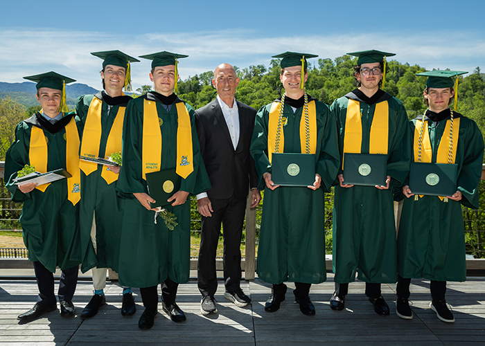 A group of students wearing graduation gowns stand with Director of Cycling Tim Hall.