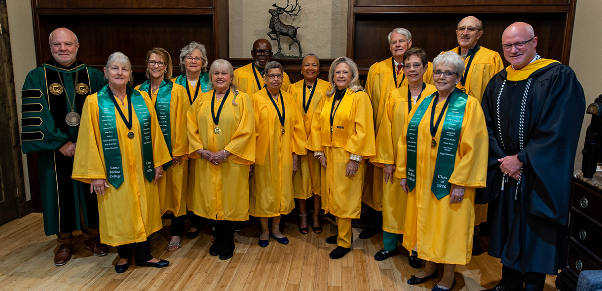 A large group of alumni wearing gold graduation gowns stands with President Lee King and Chris Finley.