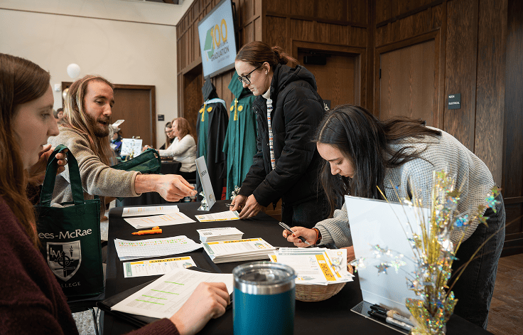 two students receiving papers about 100 Days and signing up at front table