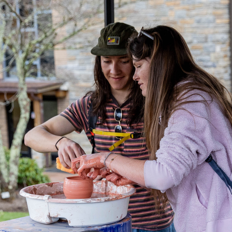 Two students working together on a pottery wheel.
