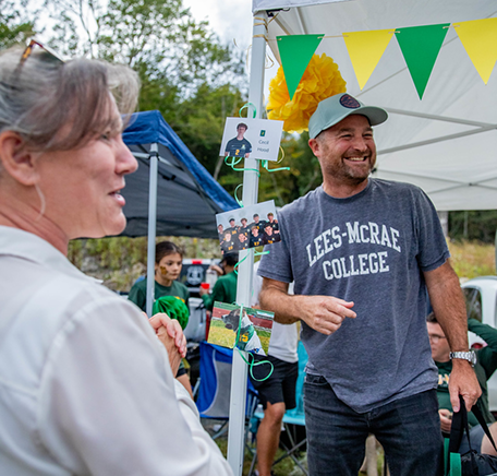 People talk and laugh under a Lees-McRae tent decorated with green and yellow pennants.