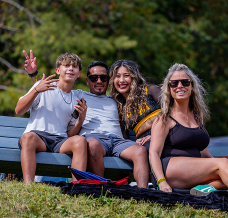 A family sits together on a grassy hillside during an outdoor campus event.