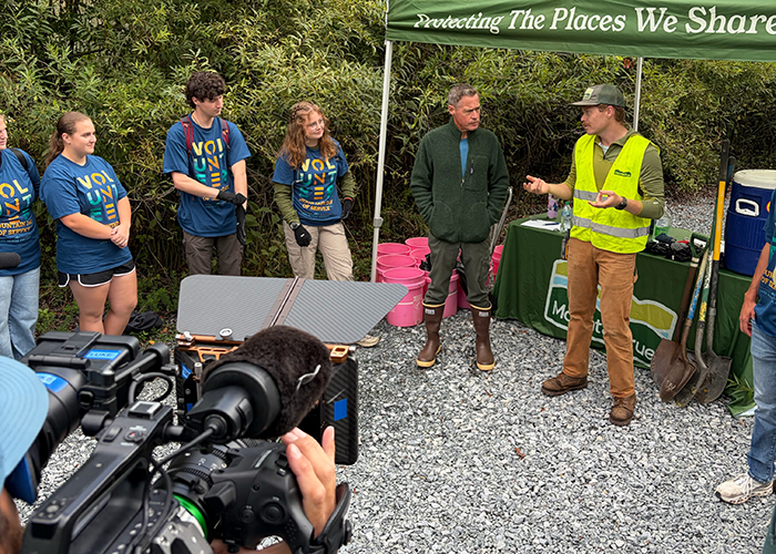 Jeff Corwin stands in the Elk Valley Preserve with a group of student volunteers. A television camera can be seen filming them in the foreground.