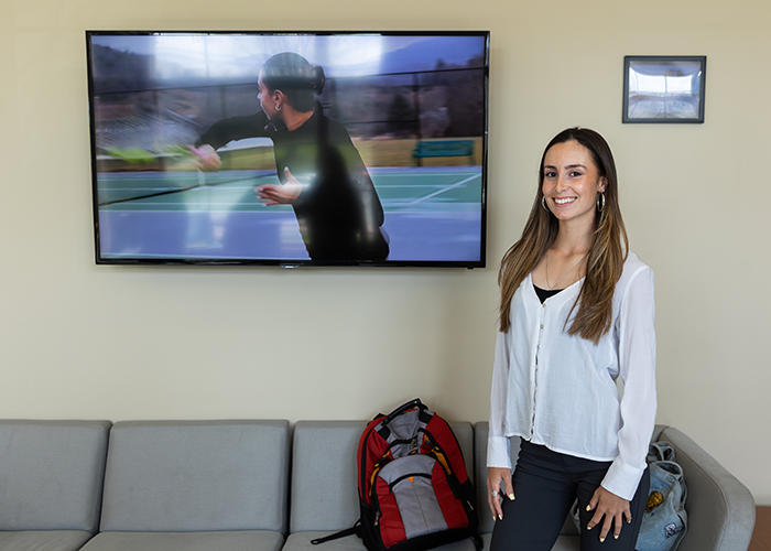 Sanchez stands in front of a television that is playing one of her videos.