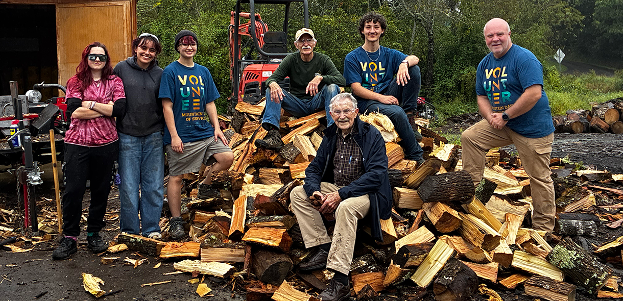 A group of volunteers pose with a pile of chopped wood.