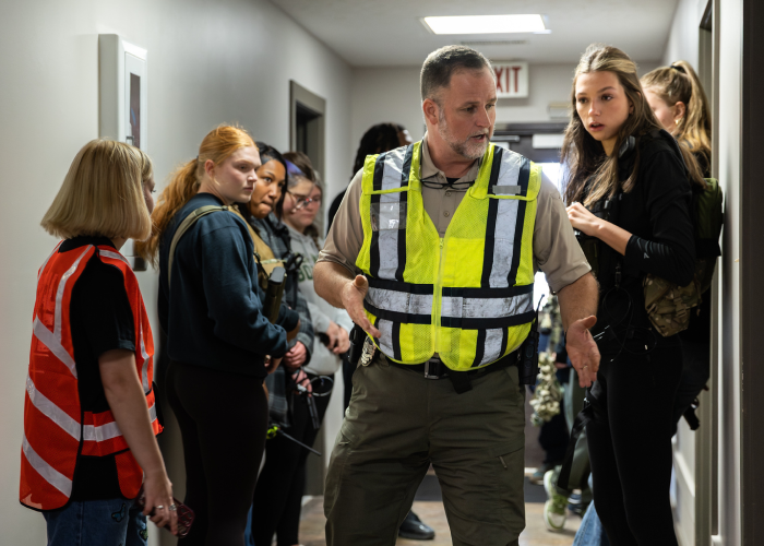 A criminal justice instructor in a reflective safety vest leads students through a training exercise.