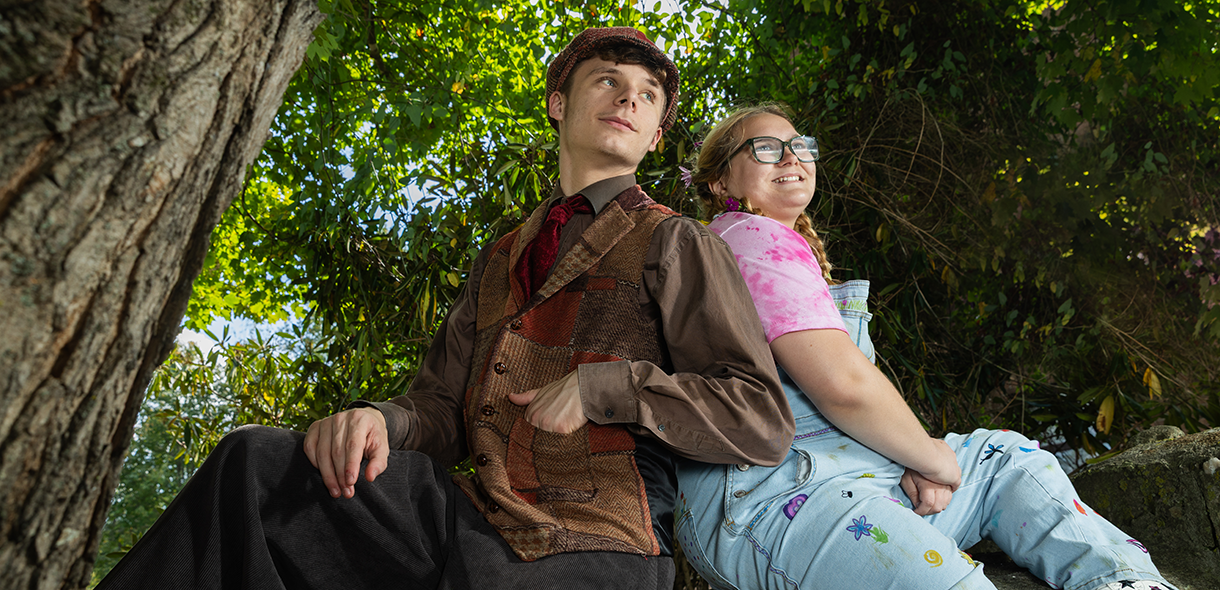 Two student actors in costume sit in a tree.