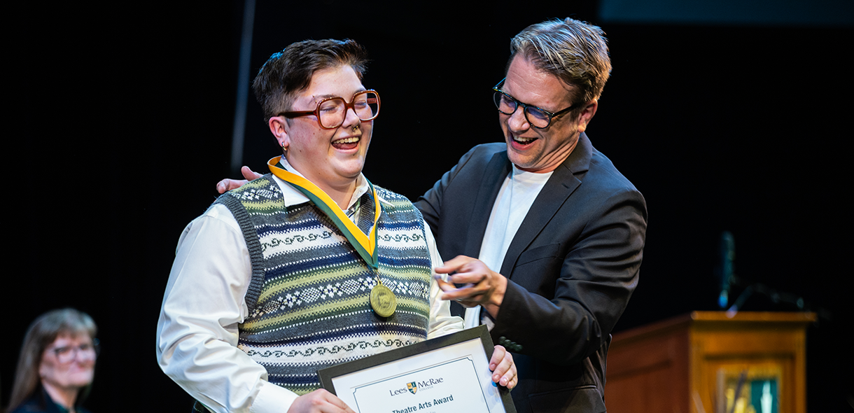 A faculty member places a medal on a smiling student who is holding a framed award certificate.