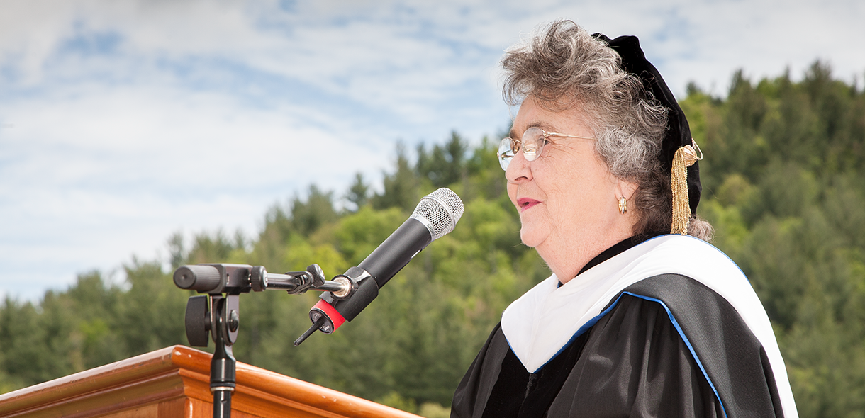Jane Stephenson wears doctoral regalia and speaks into a microphone at a podium.
