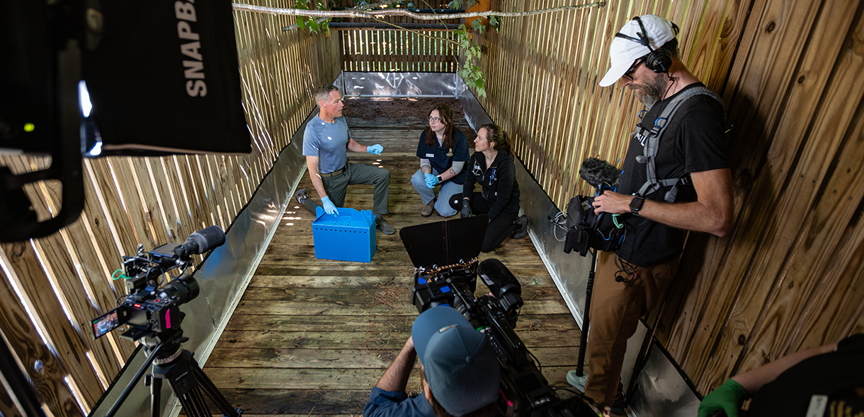 Jeff Corwin sits in front of a camera crew with a Lees-McRae student and professor.