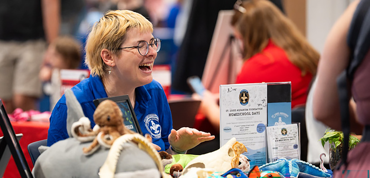 Mel Hooper laughs while sitting at a table covered with stuffed toy sea animals.