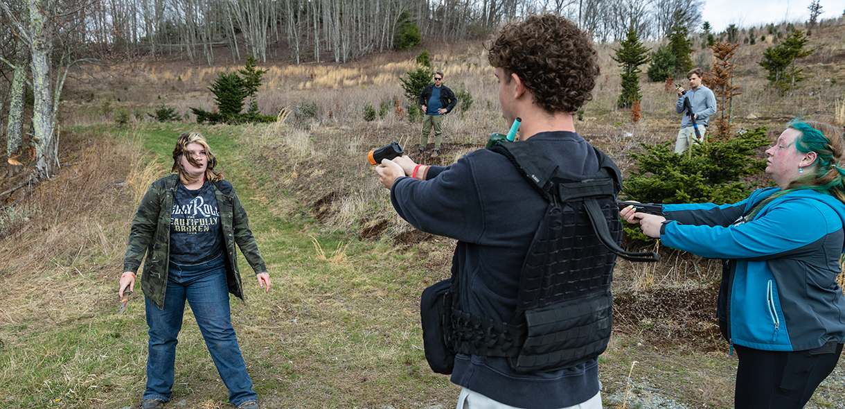 Two students acting as police officers aim fake weapons at a student acting as an assailant.