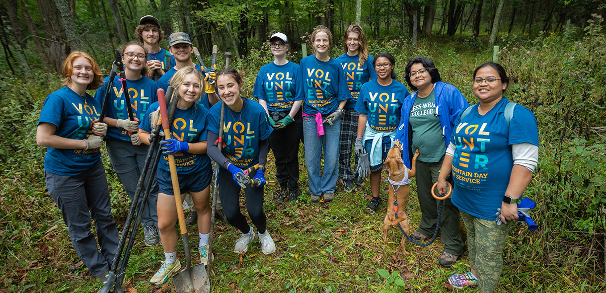 A group of volunteers wearing Mountain Day of Service shirts stand together in the woods.
