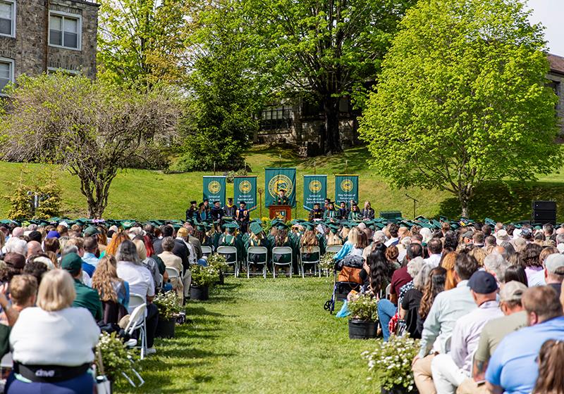 Graduates and families sit on Tate Lawn while President King addresses the crowd from a podium.