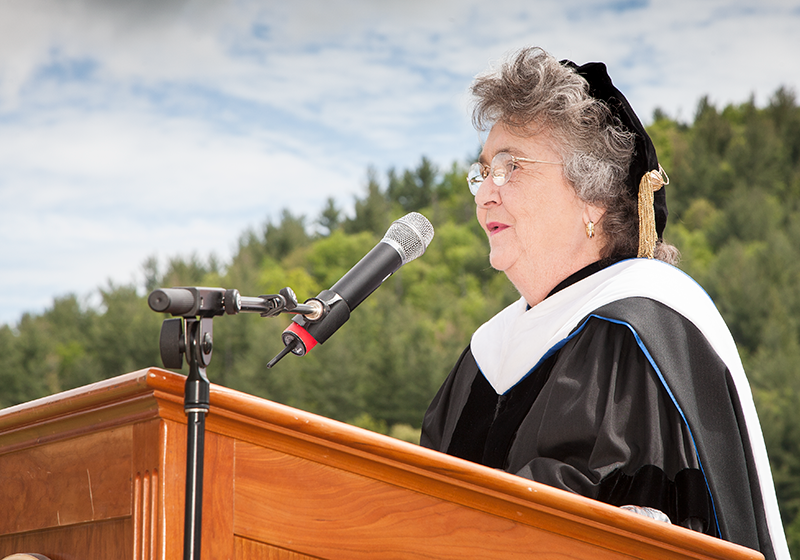 Jane Stephenson wears doctoral regalia and speaks into a microphone at a podium.