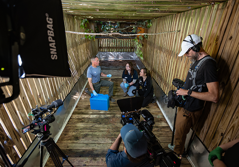 Jeff Corwin sits in front of a camera crew with a Lees-McRae student and professor.