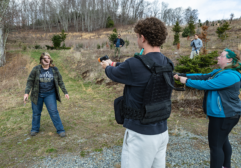 Two students acting as police officers aim fake weapons at a student acting as an assailant.