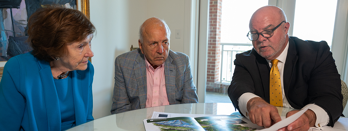 Smoky and Margaret Bissell sit at a table with President Lee King and examine building plans.