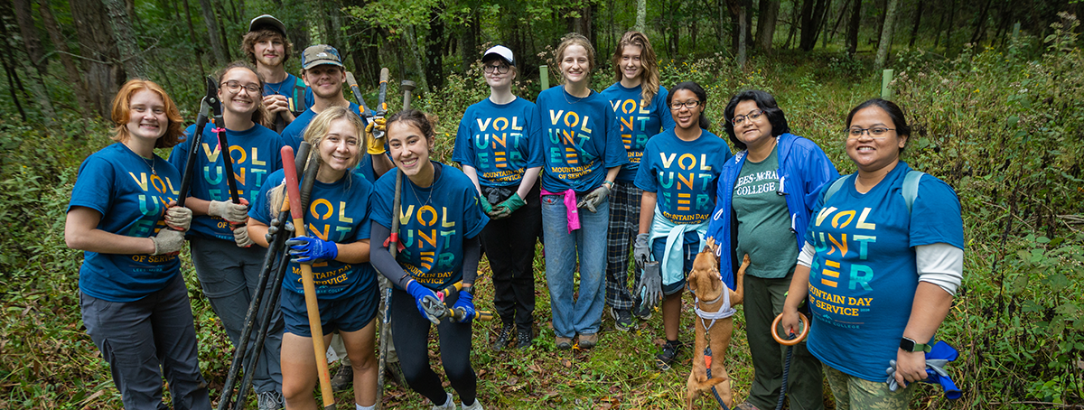 A group of volunteers wearing Mountain Day of Service shirts stand together in the woods.
