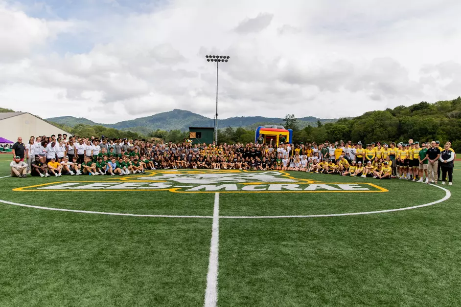 Large group of students, faculty, and staff gathered for a panoramic photo on an athletic field with the Lees-McRae logo at midfield
